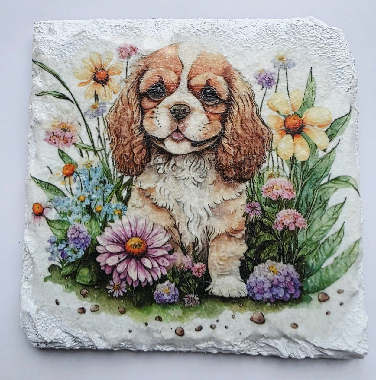 White slate coaster with a painting of a king charles spaniel puppy surrounded by flowers on a white background