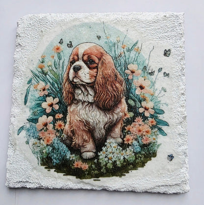 White slate coaster with a painting of a king charles spaniel puppy surrounded by flowers on a white background