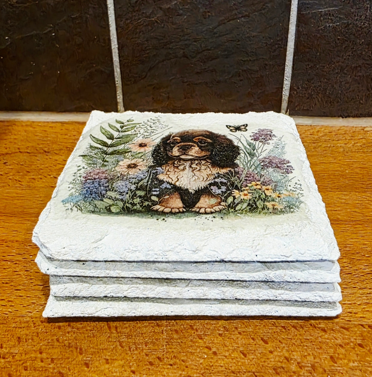 Stack of four white slate coasters with a spaniel dog and floral design on a wooden surface.