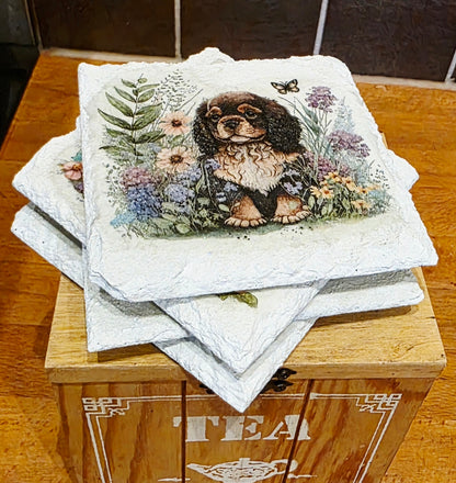 Stack of four white slate coasters with a spaniel dog and floral design on a wooden box labeled 'Tea'.