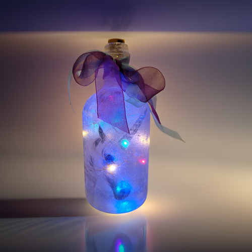 Gin bottle, lit up with multi-coloured cork lights. Unicorn detailing on the front of the bottle. Purple organza ribbon tied around the neck of the bottle