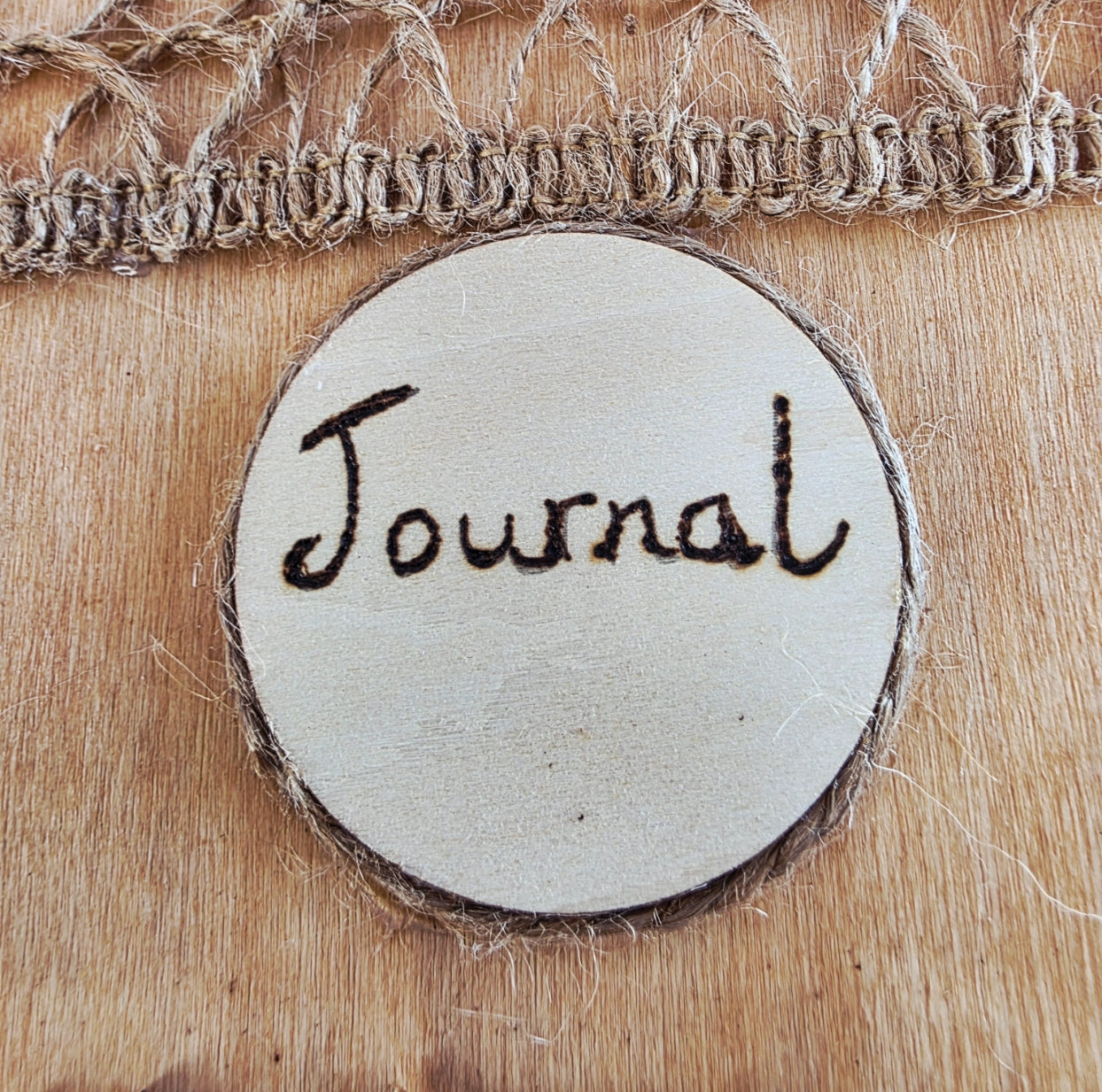 Round wooden sign with 'Journal' engraved on it, placed on a wooden surface. jute twine around the edge