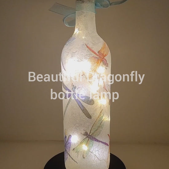 Rotating wine bottle decorated with Dragonflies. Bottle is lit up using cork LED lights. Blue organza ribbon