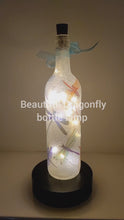 Load and play video in Gallery viewer, Rotating wine bottle decorated with Dragonflies. Bottle is lit up using cork LED lights. Blue organza ribbon
