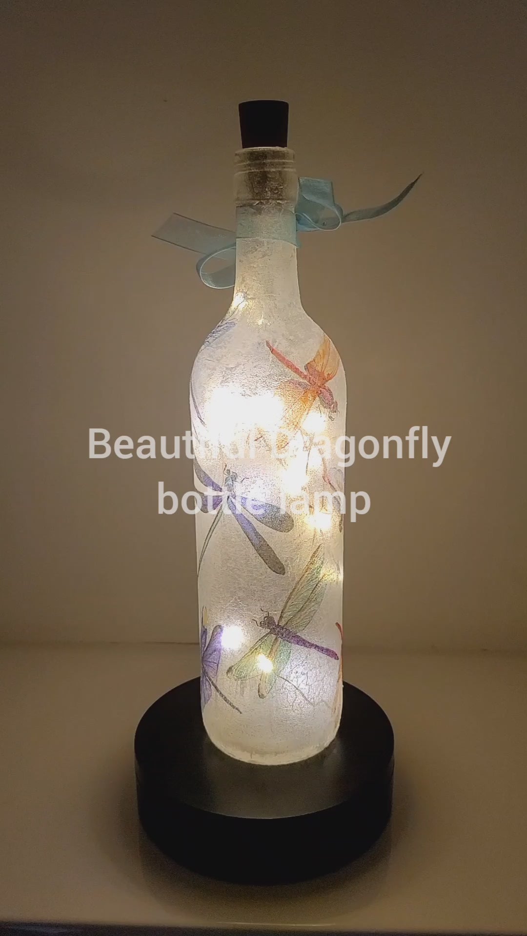Rotating wine bottle decorated with Dragonflies. Bottle is lit up using cork LED lights. Blue organza ribbon