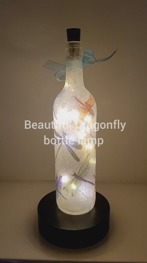 Rotating wine bottle decorated with Dragonflies. Bottle is lit up using cork LED lights. Blue organza ribbon