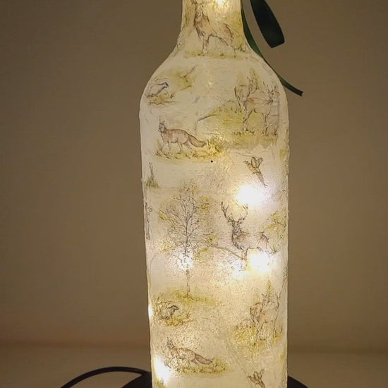 Rotating example of a Lit up wine bottle with countryside detailing, cork LED lights and green bow