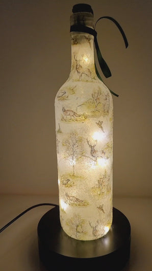 Rotating example of a Lit up wine bottle with countryside detailing, cork LED lights and green bow