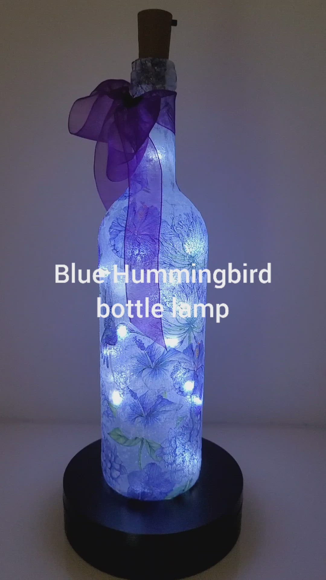 Rotating Lit up bottle with blue Hummingbird and blue flowers  detail. Cork lights. Purple ribbon