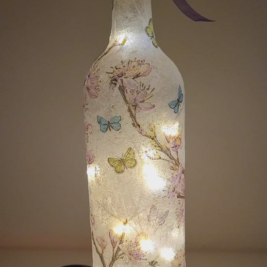 Rotating lit up wine bottle with flower and butterfly detail. Purple bow 