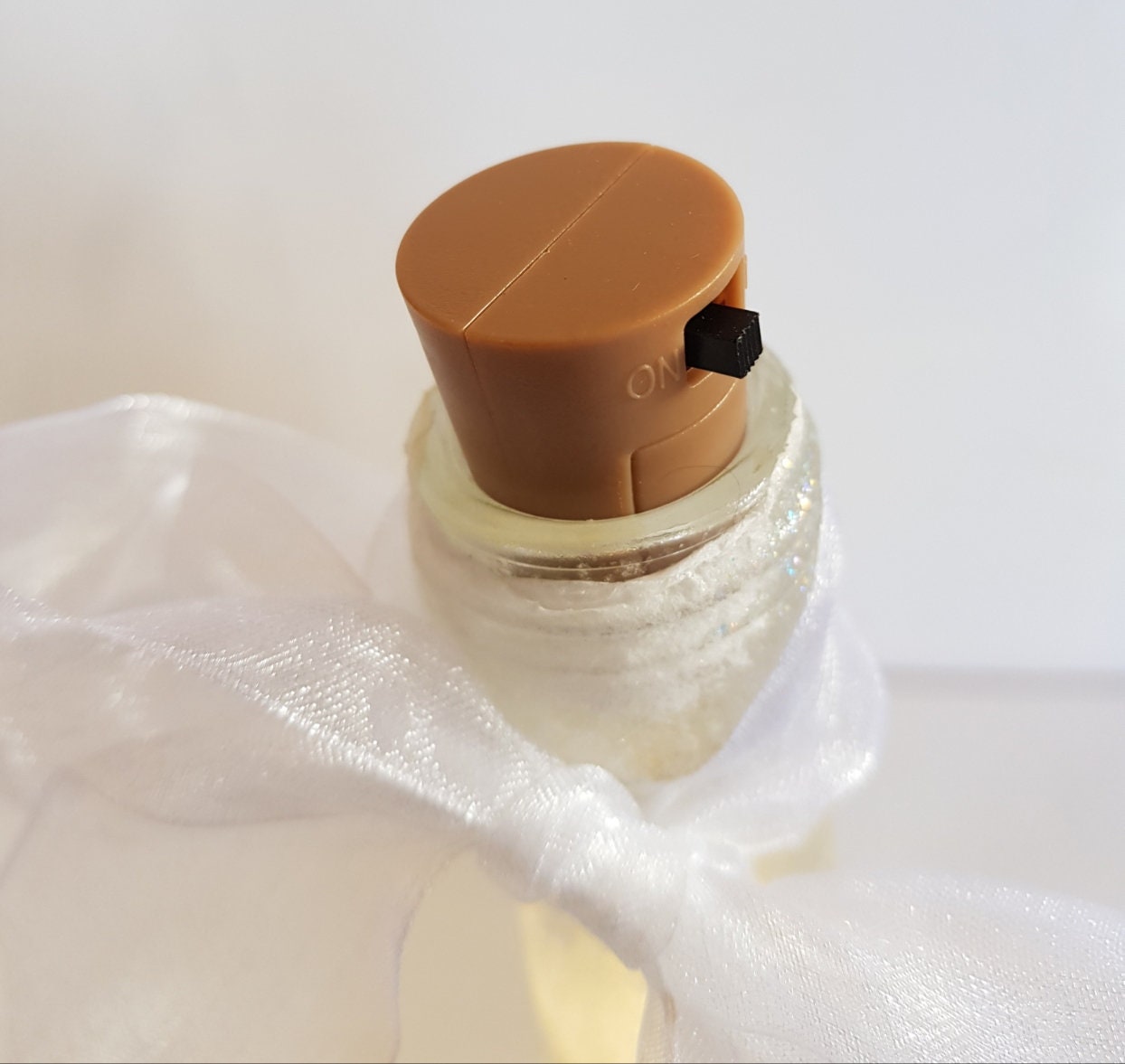 Brown plastic cork in top of bottle showing on/off switch. White bow